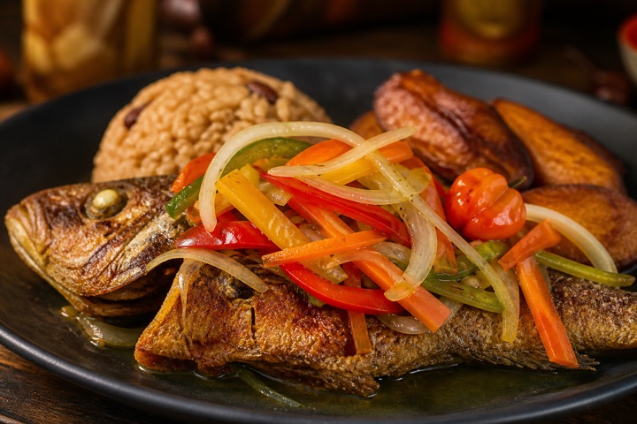 Escovitch Fish: Fried snapper fish decorated with bell peppers, onions, carrots, and hot peppers in vinegar. Served with rice, cabbage and plantain.