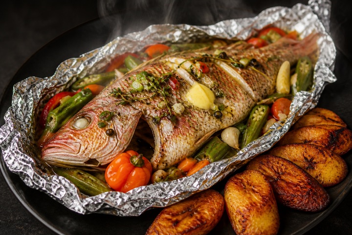 Roast Fish: Snapper fish in foil paper with okra & callaloo cooked on the grill. Served with rice, cabbage and plantain.